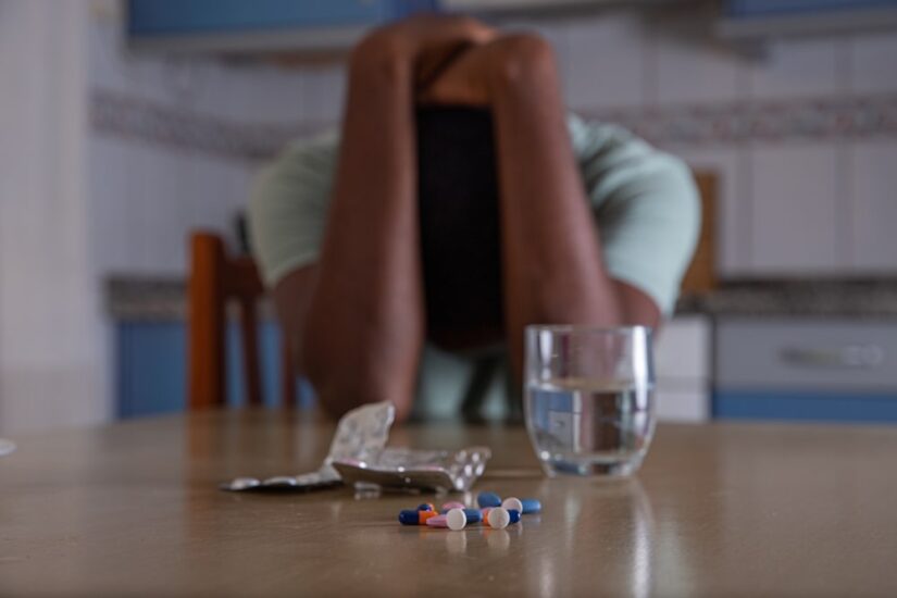 Person Holding His Hand Being Sad With Pils And A Glass Of Water In Front Of Him